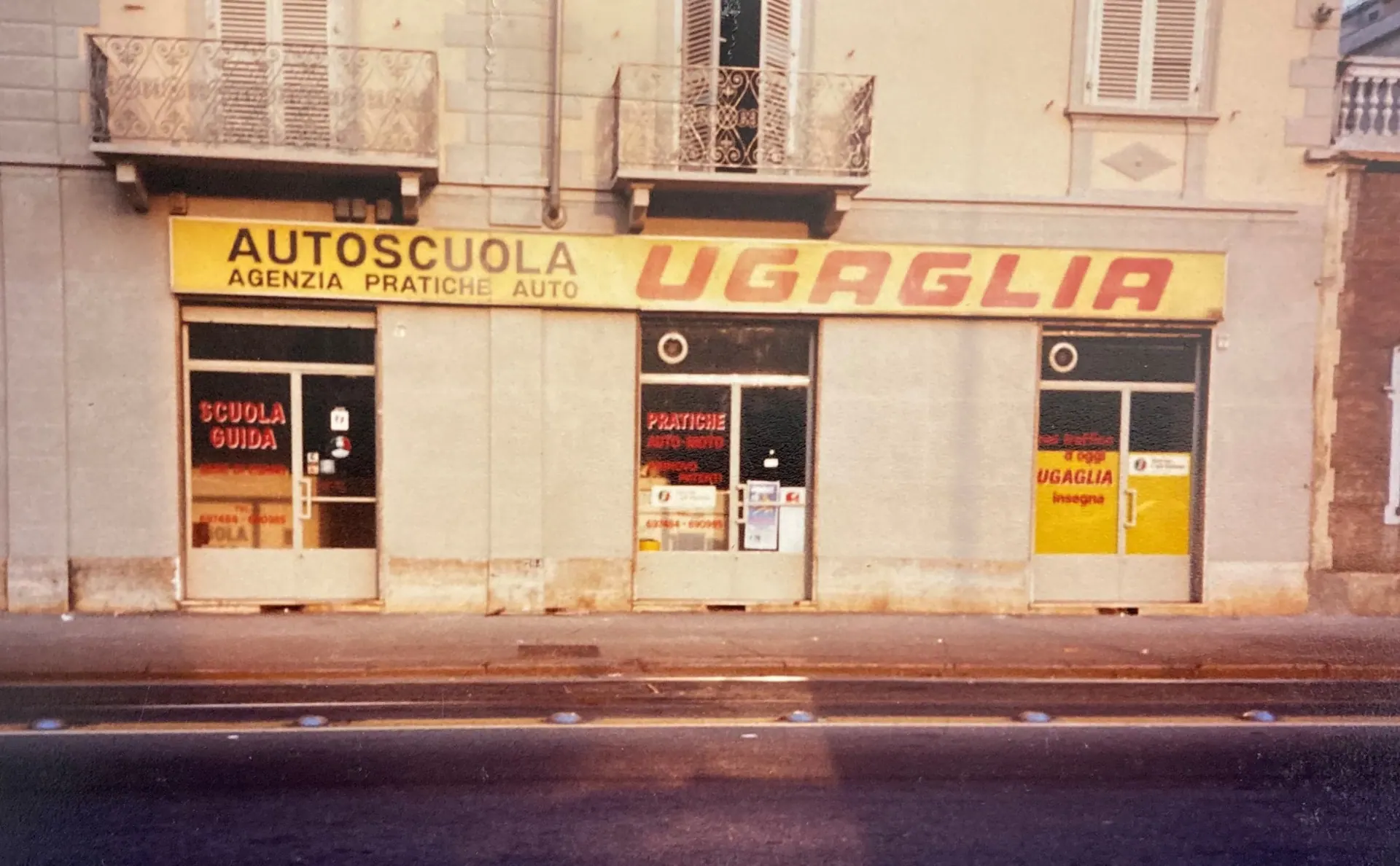La vetrina di Autoscuola Ugaglia nel 1980, con la lunga insegna gialla «Autoscuola – Agenzia pratiche auto – Ugaglia»